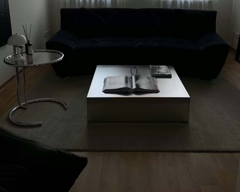 Brushed Q Couchtisch aus gebürstetem Edelstahl in minimalistischem Wohnzimmer mit dunklem Sofa und ruhiger Abendstimmung