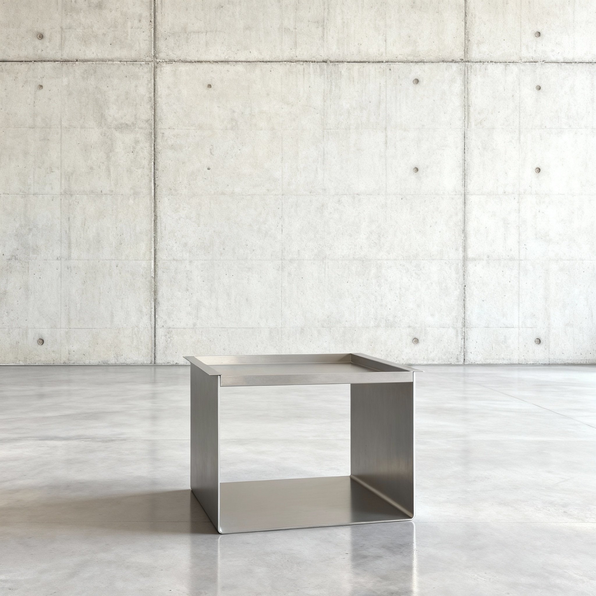 Tray Table Brushed C Beistelltisch in gebürstetem Edelsthahl auf grauen Betonboden vor grauer Betonwand mit Löchern