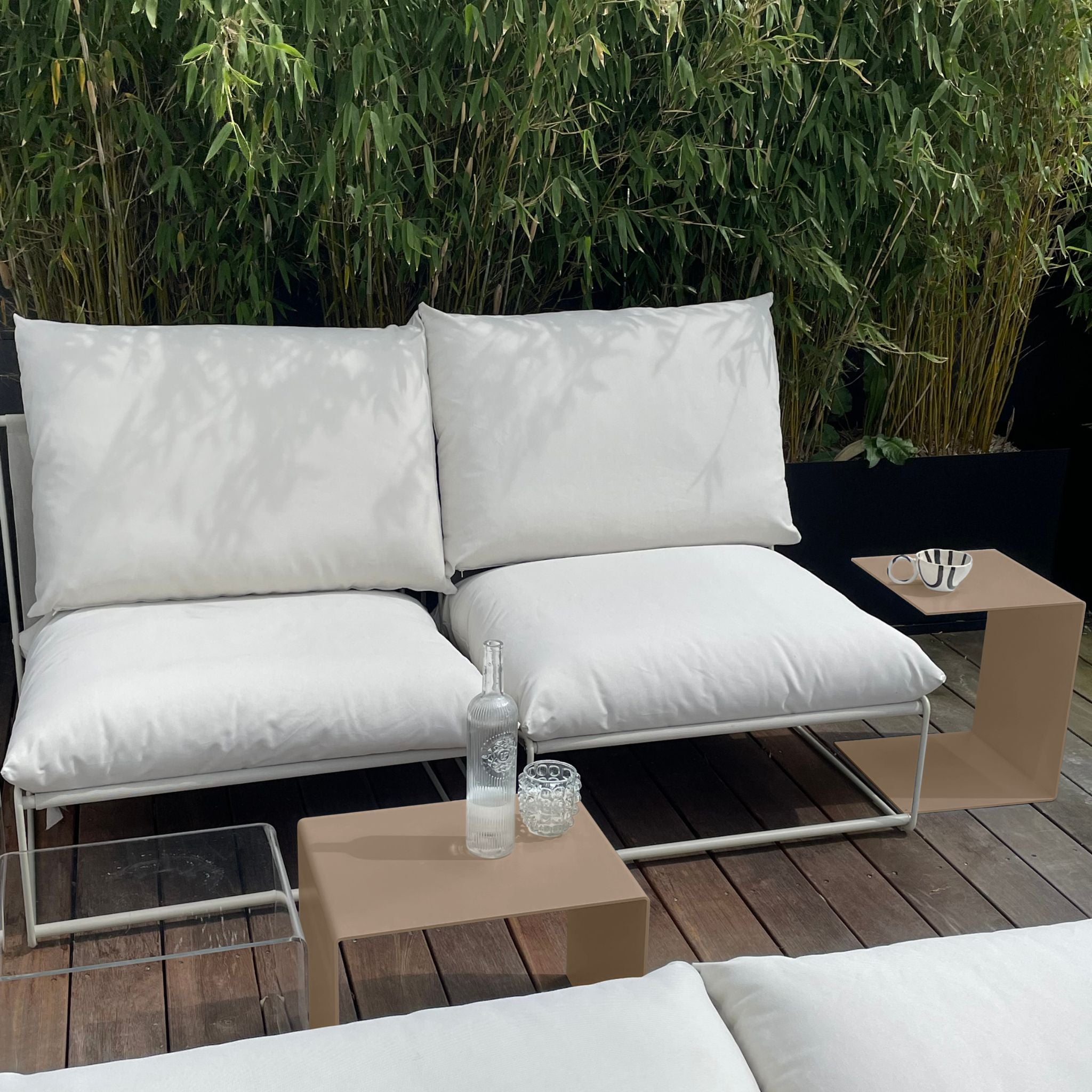 Graubeiger Beistelltisch und Couchtisch neben weißem Outdoor-Loungesofa auf Holzterrasse