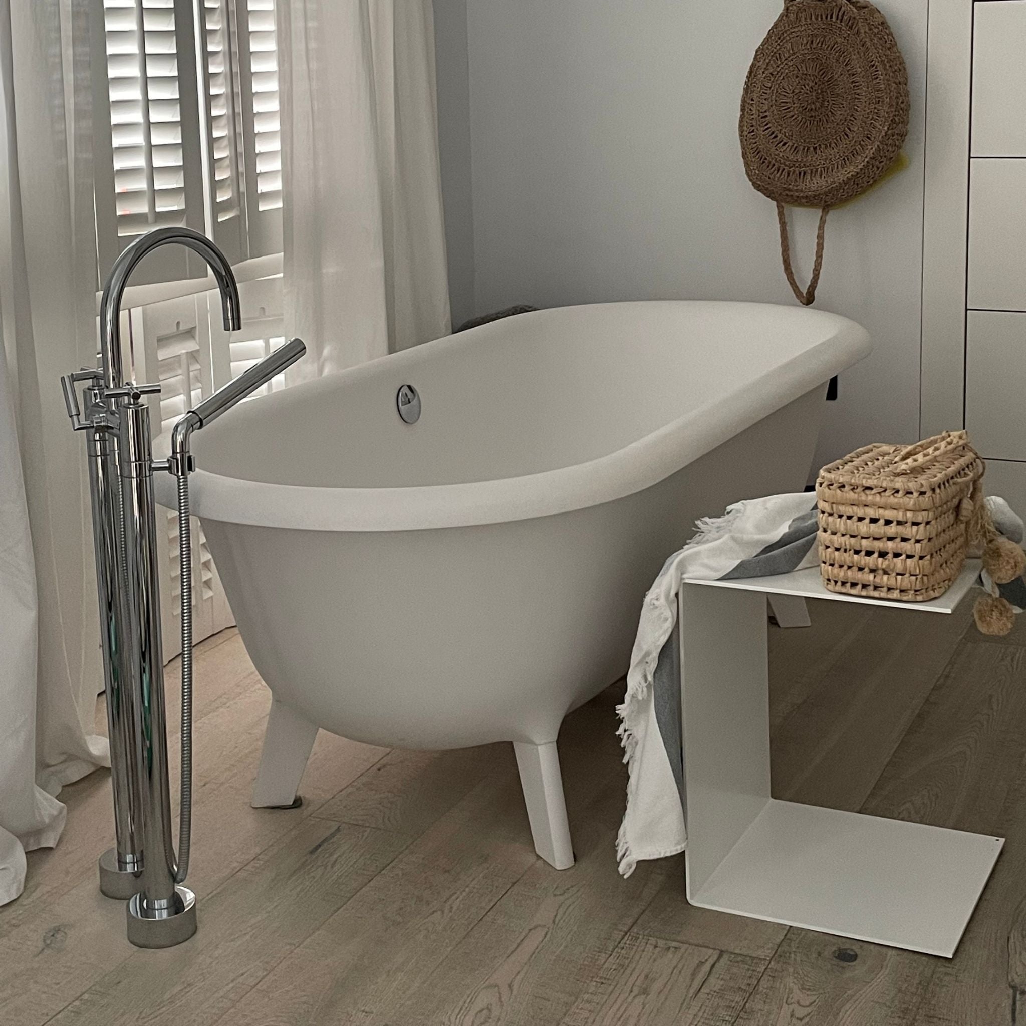 Weißer Beistelltisch als Ablage neben freistehender Badewanne in modernem Badezimmer mit Holzboden
