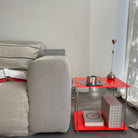 Leuchtroter Beistelltisch aus Edelstahl neben hellem Sofa, dekoriert mit Designobjekten und Büchern
