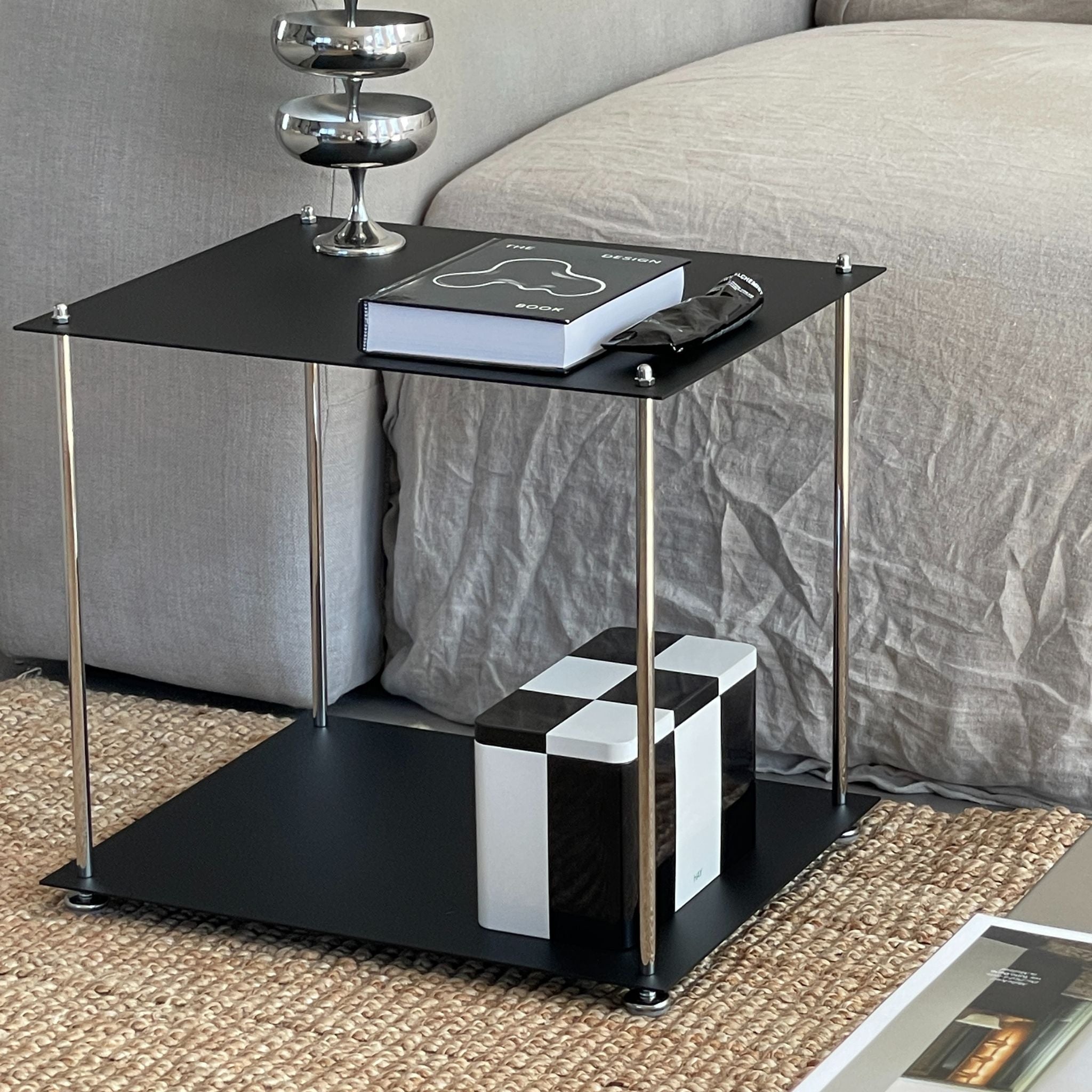 MODULUM Beistelltisch in Schwarz matt mit Pulverbeschichtung vor Sofa, dekoriert mit Buch und Designobjekten