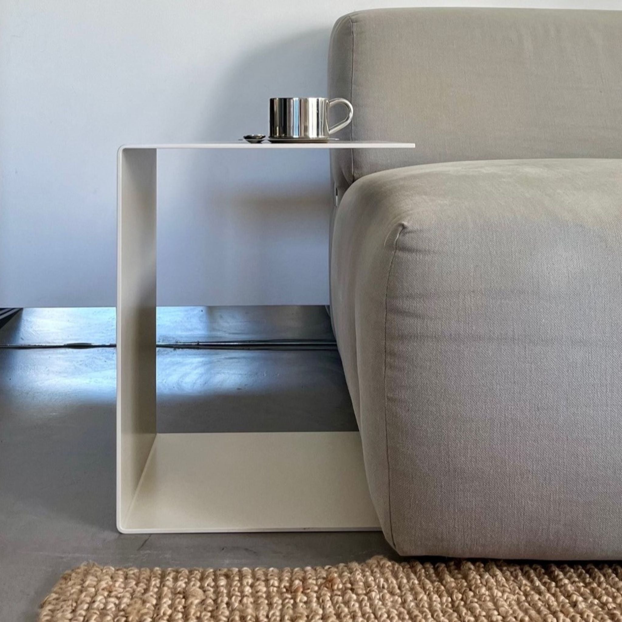 Cremeweißer BIG C Beistelltisch aus Stahl am grauen Sofa mit Tasse und Löffel, eingesetzt als Sofatisch auf hellem Teppich