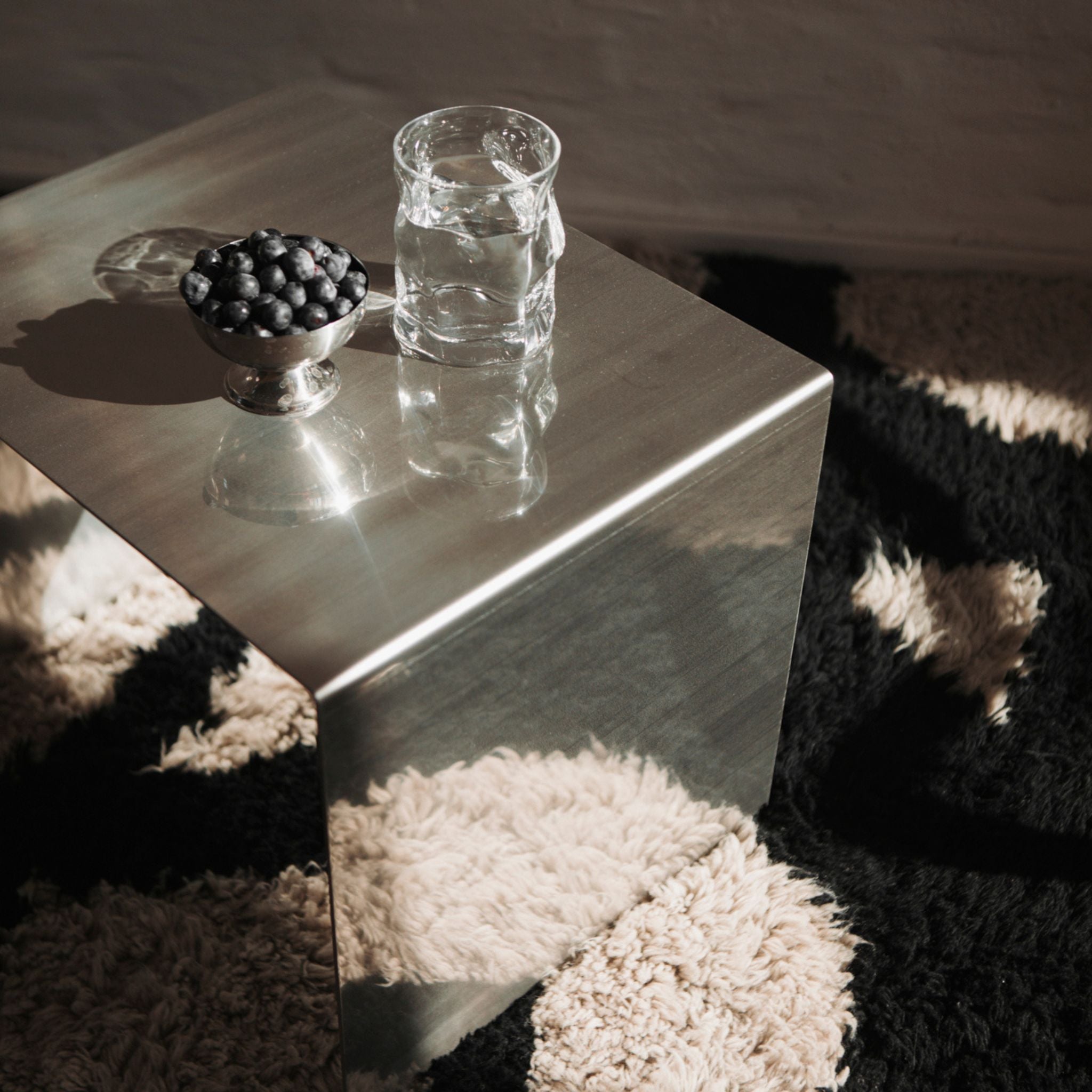 Minimalistischer Edelstahl-Hocker mit Wasser und Blaubeeren auf Teppich im Sonnenlicht