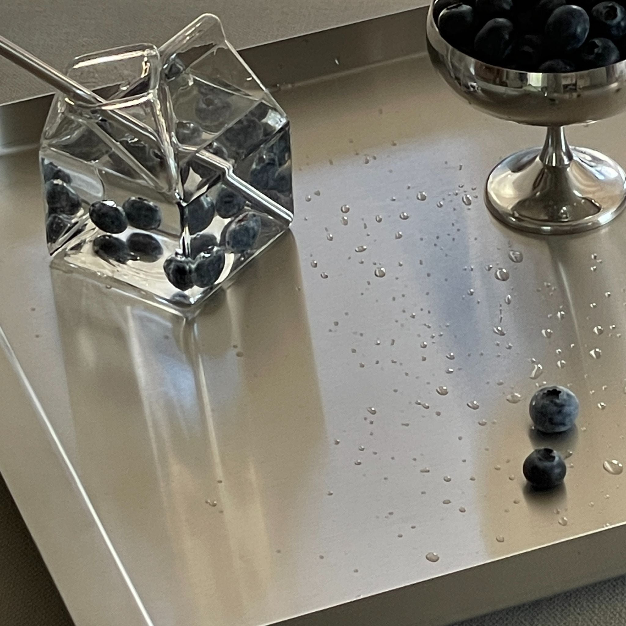 nahaufnahme edelstahl tablett mit blaubeeren und wassertropfen im sonnenlicht