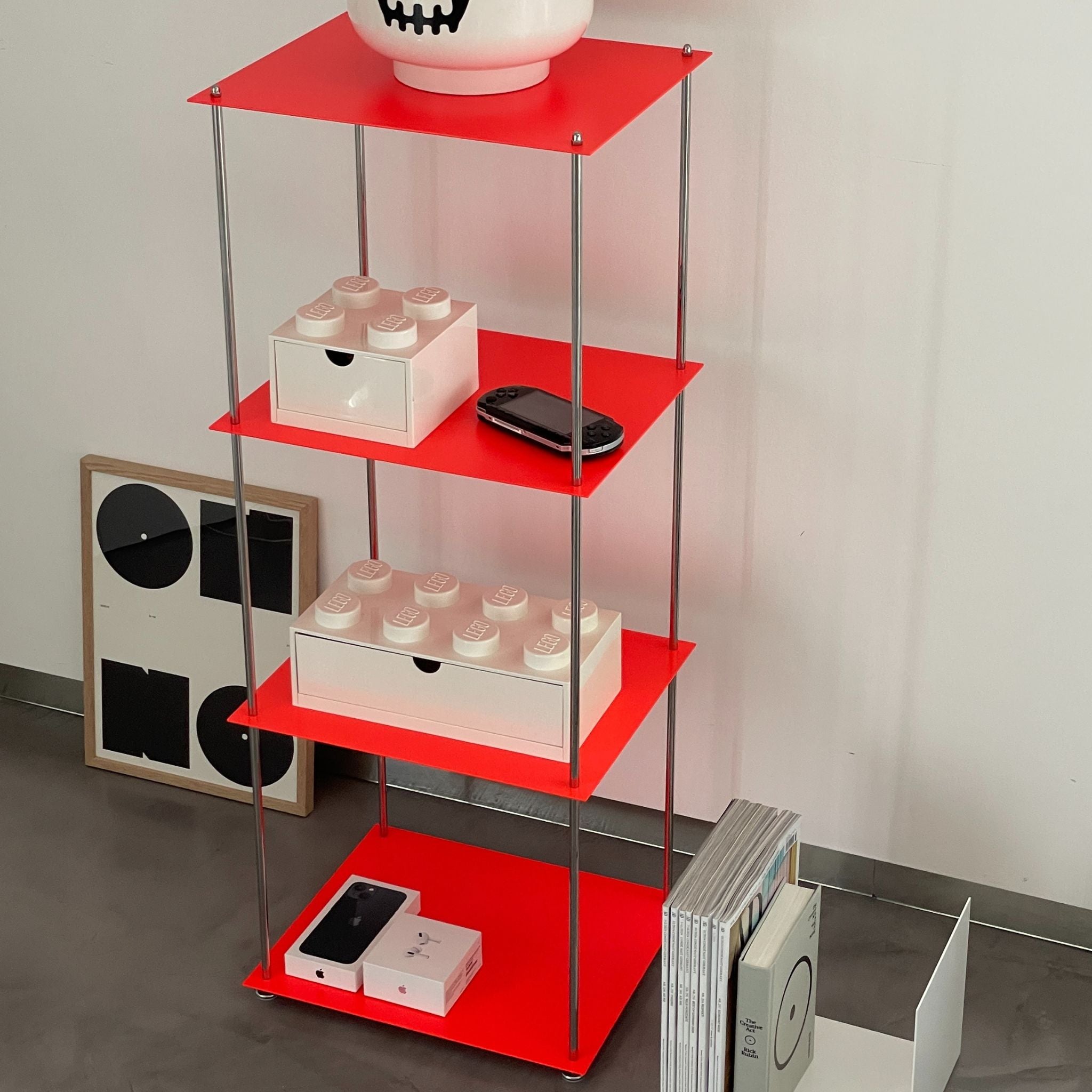 Rotes Regal mit Lego-Box, Konsole und Designmagazinen
