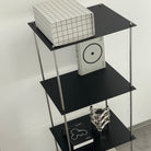 Modernes schwarzes Regal von MO INTERIORS mit Designbuch, Kerzenhalter und Rasterbox in minimalistischem Interieur