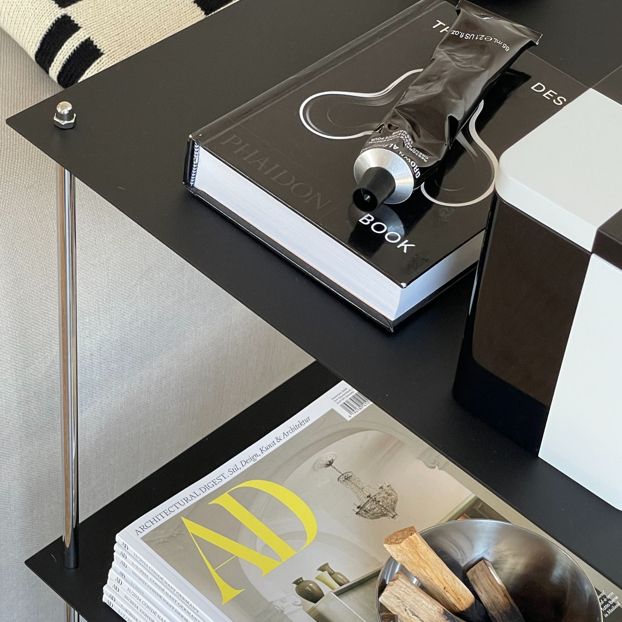 Detailansicht eines schwarzen pulverbeschichteten Regals mit Designbuch und Deko im Wohnzimmer