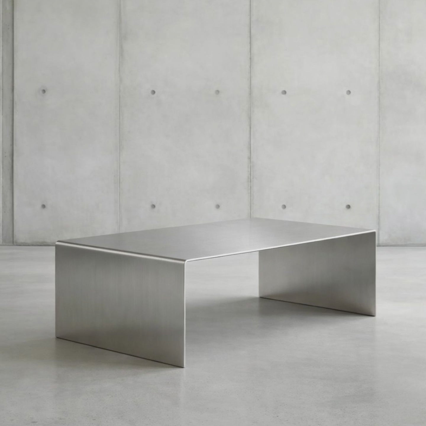 360 Grad Drehung Brushed C Long Couchtisch aus gebürstetem Edelstahl in minimalistischer Studioinszenierung vor Betonwand