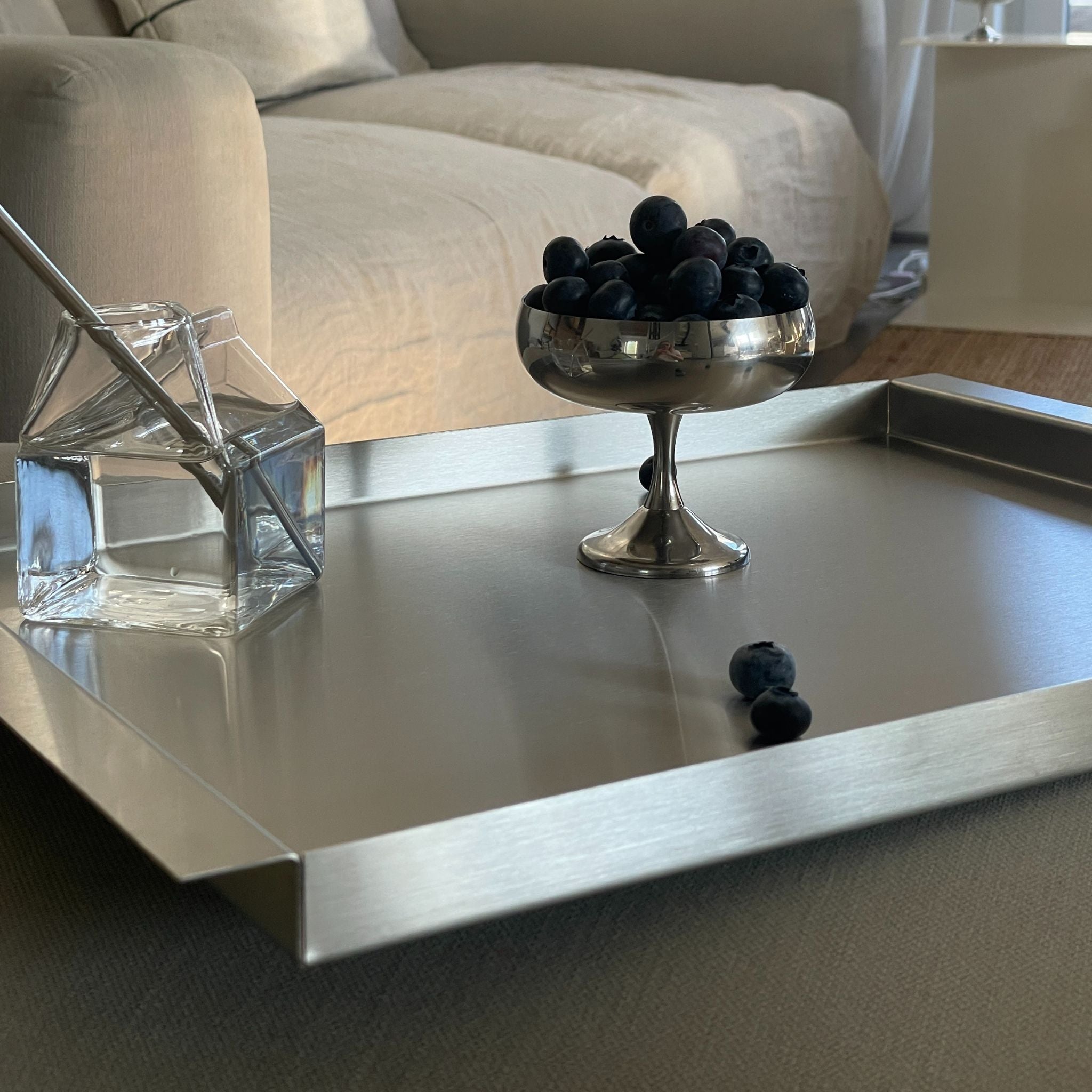 modernes tablett aus edelstahl mit wasserglas und silberschale auf wohnzimmersofa