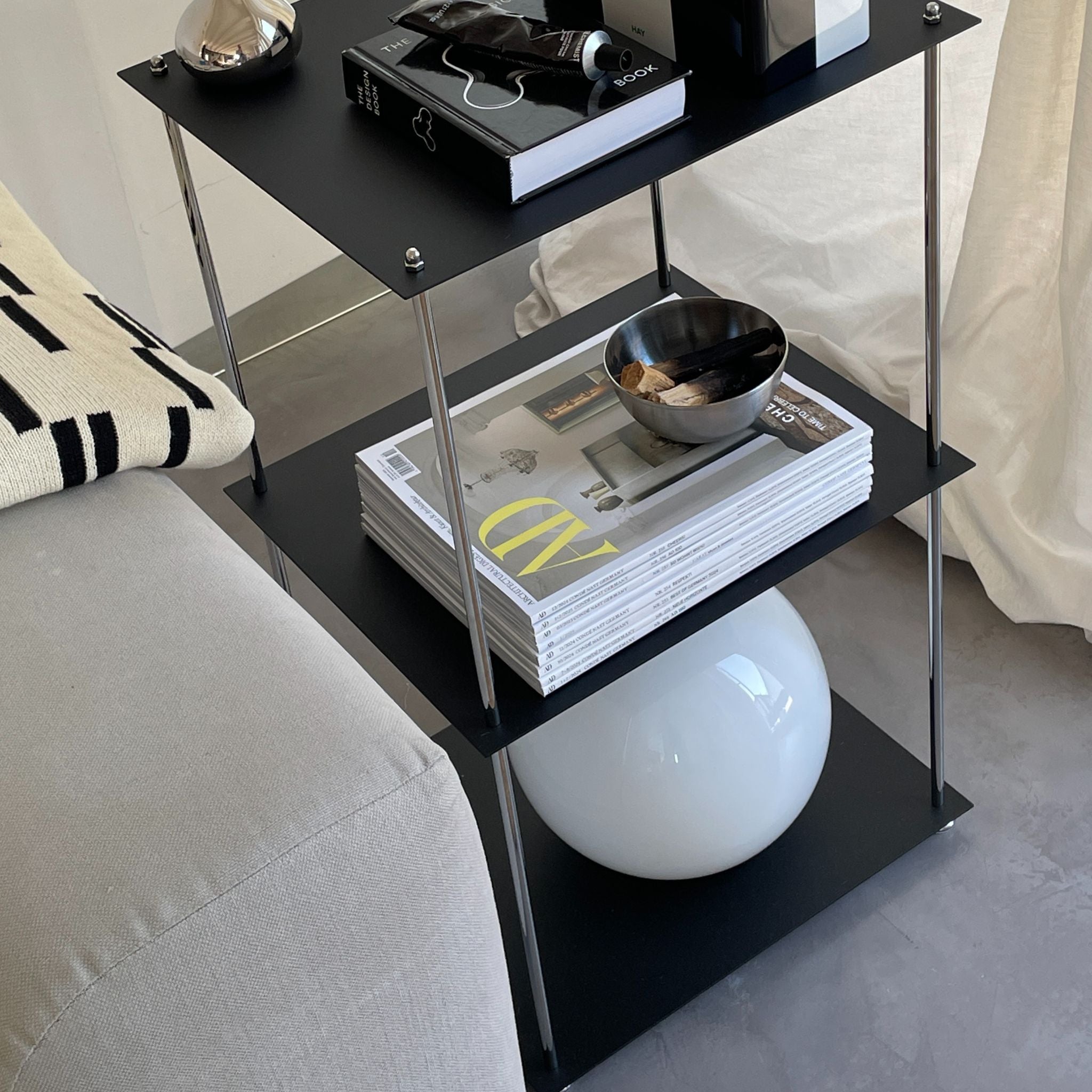 Schwarzes pulverbeschichtetes Regal mit Wohnaccessoires neben hellem Sofa im modernen Wohnzimmer