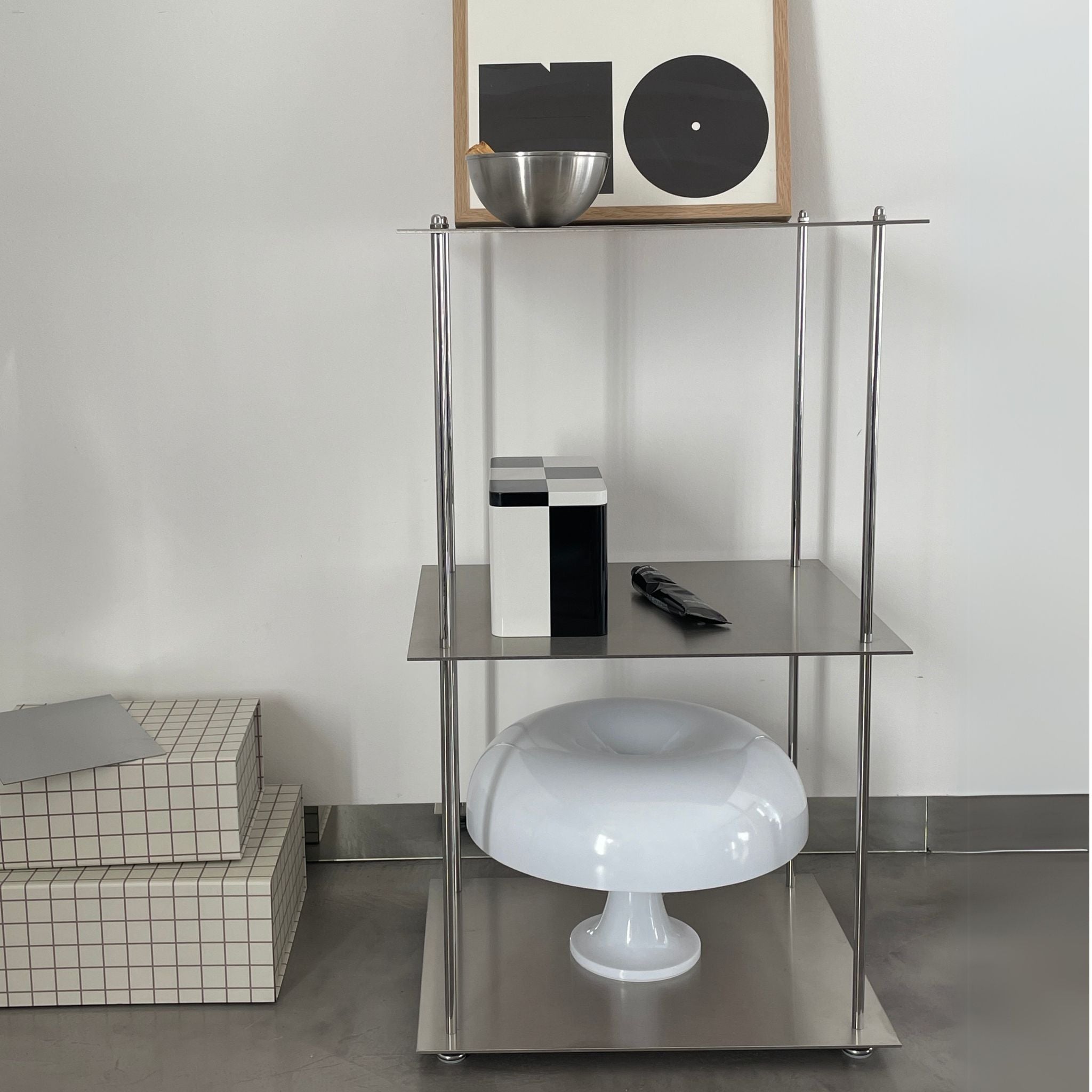 Modulares Edelstahl-Regalsystem mit Designobjekten und Pilzlampe vor einer weißen Wand