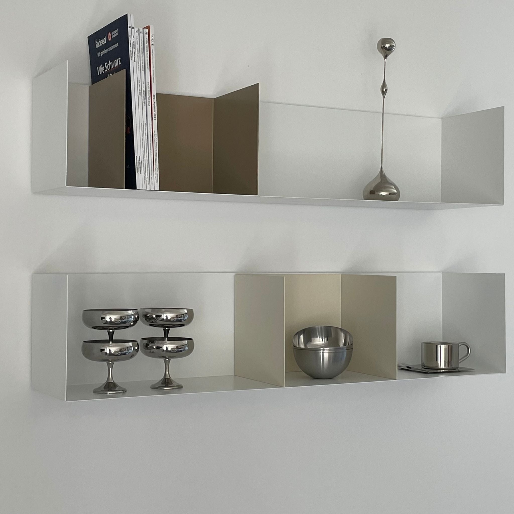 Weißes Wandregal mit Buchstützen in Cremeweiß und Graubeige, dekoriert mit Edelstahl-Accessoires